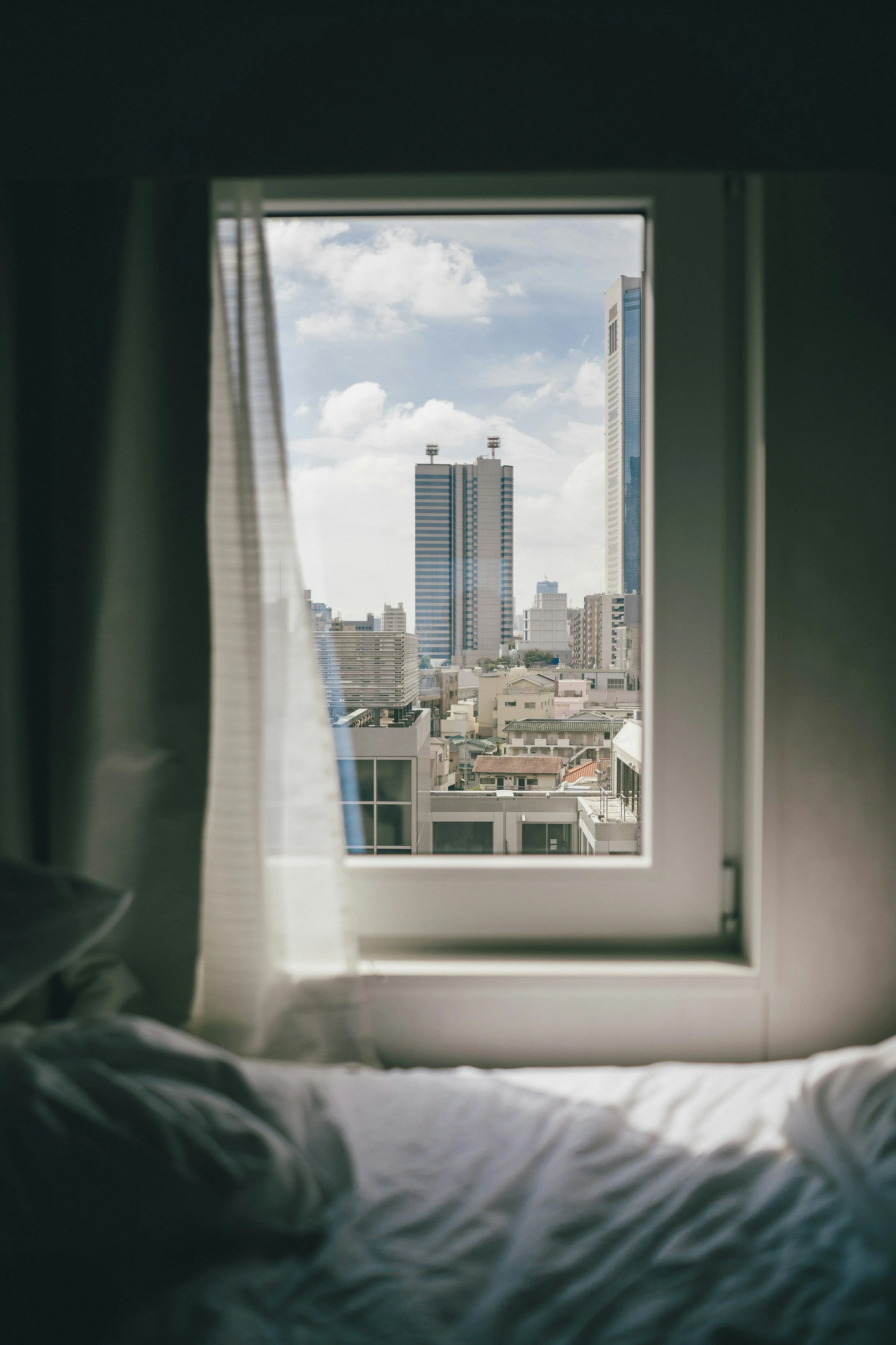 A bedroom window overlooking a city at dusk